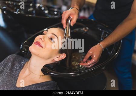Coupe courte de coiffeur méconnaissable lavant les cheveux blonds de sa cliente féminine souriante positive dans le salon de beauté. Photo de haute qualité Banque D'Images