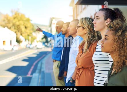 Tous alignés de suite. un groupe d'amis debout et regardant dans la distance à côté d'une rue à l'extérieur. Banque D'Images