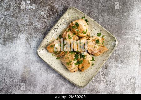 Cuisses de poulet à l'ail cuites au four avec des herbes sur une assiette carrée sur fond sombre. Vue de dessus, plan d'appartement Banque D'Images