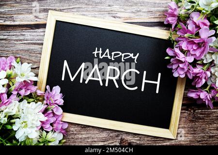 Happy March texte typographique écrit sur tableau noir en bois avec bouquet de fleurs sur fond en bois Banque D'Images