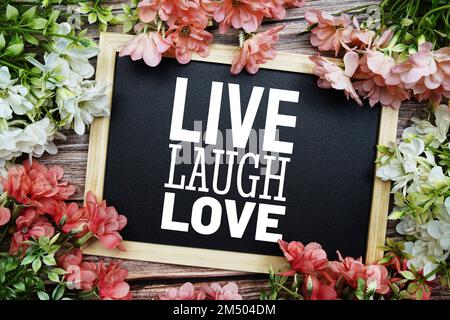Texte typographique Live Laugh Love écrit sur tableau noir en bois avec bouquet de fleurs sur fond en bois Banque D'Images