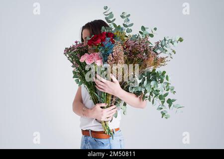 Les fleurs sont le langage de l'amour. Photo en studio d'une femme méconnue tenant des fleurs sur un fond gris. Banque D'Images