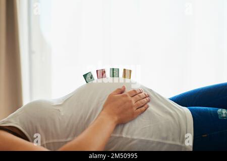 Ses bébés ont été mis sur le cerveau. une femme enceinte non identifiable allongé sur son lit avec des blocs orthographes bébé disposés sur son ventre. Banque D'Images