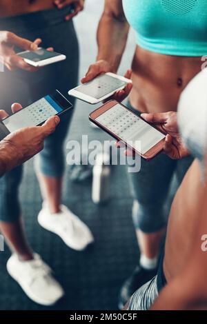 Tous ont eu une application pour synchroniser leurs programmes d'entraînement. Gros plan d'un groupe de personnes utilisant leur téléphone portable ensemble à la salle de gym. Banque D'Images