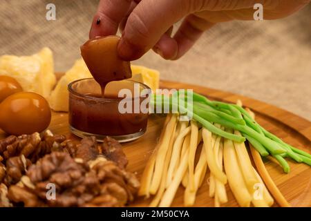 Quelqu'un trempent un morceau de fromage dans le miel sur un fond de variétés variées de fromage Banque D'Images