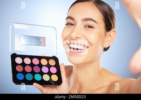 Visage selfie, beauté et femme avec kit de maquillage en studio isolé sur fond bleu. Soin de la peau, produit cosmétique et prise de modèle de femme heureuse Banque D'Images