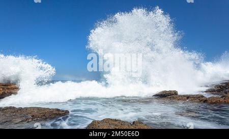 Vagues de rochers s'écrasant l'eau de mer de l'océan blanc explosant pulvérisez de la puissance dans le ciel bleu le long de la côte rocheuse gros plan Photographie. Banque D'Images