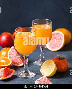 Jus d'agrumes dans deux verres et mandarine de fruits frais, orange, pamplemousse et citron sur fond gris foncé. Vue avant Banque D'Images