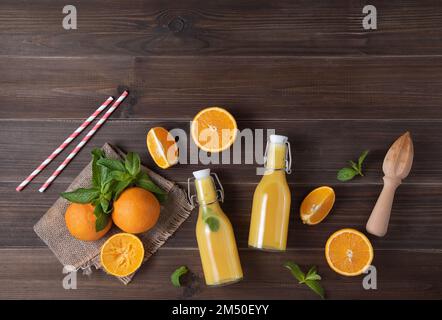 Concept plat avec jus d'orange frais maison à la menthe dans deux bouteilles avec agrumes sur fond de bois brun. Vue de dessus et espace de copie Banque D'Images