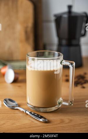Tasse de café aromatique fraîchement préparé avec du lait sur la table de cuisine avec une cafetière et des grains épars. Le concept d'un matin tôt Banque D'Images