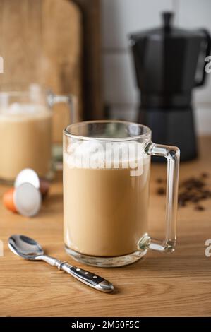 Deux tasses de café aromatique fraîchement préparé avec du lait sur la table de cuisine avec une cafetière et des grains épars. Le concept d'un petit déjeuner tôt le matin Banque D'Images