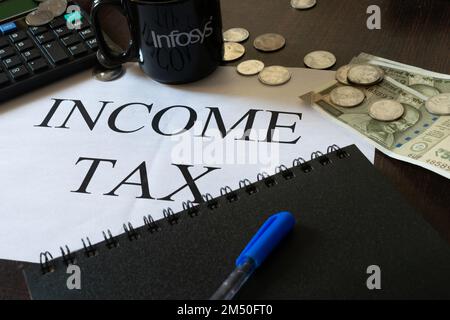 Photo de l'impôt sur le revenu écrit sur une page avec calculatrice, journal, argent, stylo et une tasse d'Infosys. Budget, déclaration de revenus, production, entreprise, emploi, savi Banque D'Images