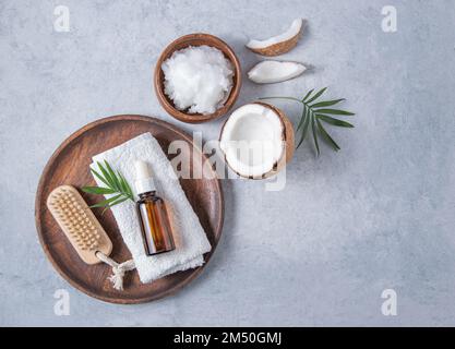 concept de soins bio. Huile de noix de coco saine avec une brosse en bois et une moitié de noix de coco dans une assiette sur fond bleu. Vue de dessus et espace de copie i Banque D'Images