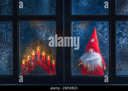 Noël, nouvel an, composition d'hiver. Gnome de Noël et bougies derrière une fenêtre gelée à motifs givré Banque D'Images