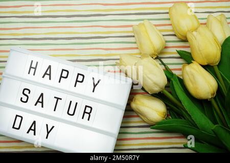 Vue du haut Happy Saturday Text in Light Box Flat Lay avec bouquet de fleurs de tulipe Banque D'Images