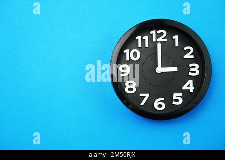 horloge ronde noire affichant cinq heures sur fond bleu Banque D'Images