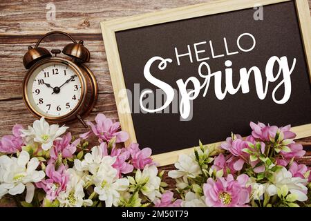 Texte typographique Hello Spring écrit sur tableau noir en bois avec bouquet de fleurs sur fond en bois Banque D'Images