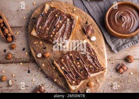 Planche de pain avec pâte de chocolat et bonbons de fête saupoudrer et noisettes sur fond de bois. Nourriture populaire de dessicer. Vue de dessus. Banque D'Images