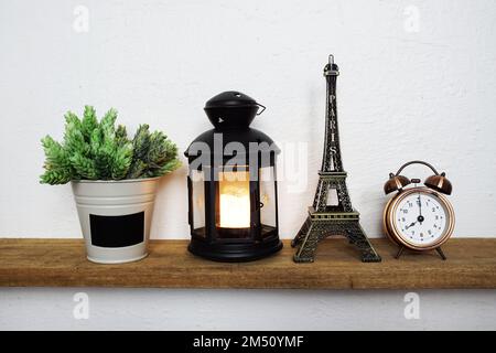 Statue de la tour Eiffel et lanterne noire avec bougie LED et réveil sur des étagères en bois Banque D'Images