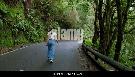 Une femme marche le long d'une route asphaltée dans une forêt dense. Arbres surcultivés dans la forêt d'arbres de Laurier ou la jungle, parc national d'Anaga, Tenerife, îles Canaries Banque D'Images