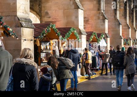 Les acheteurs de Noël au marché de Noël de Winchester avec des étals entre les contreforts volants en pierre de la cathédrale gothique de Winchester, Angleterre, Royaume-Uni Banque D'Images