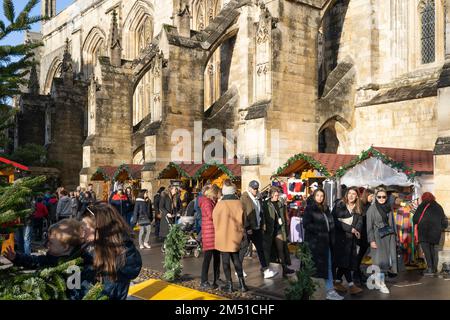 Les acheteurs de Noël au marché de Noël de Winchester avec des étals entre les contreforts volants en pierre de la cathédrale gothique de Winchester, Angleterre, Royaume-Uni Banque D'Images