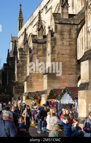 Les acheteurs de Noël au marché de Noël de Winchester avec des étals entre les contreforts volants en pierre de la cathédrale gothique de Winchester, Angleterre, Royaume-Uni Banque D'Images