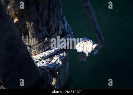 Corde accrochée à un clou dans un poteau d'amarrage près de la rive d'un lac vu de près Banque D'Images