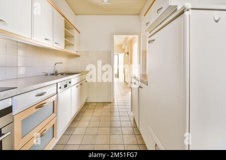 une cuisine avec des armoires blanches et des boiseries sur les murs, ainsi que le sol carrelé dans un espace ouvert Banque D'Images