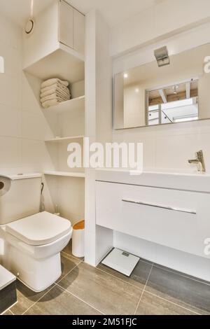une salle de bains moderne avec toilettes, lavabo et miroir dans le mur d'angle à droite est une étagère ouverte pour les serviettes Banque D'Images
