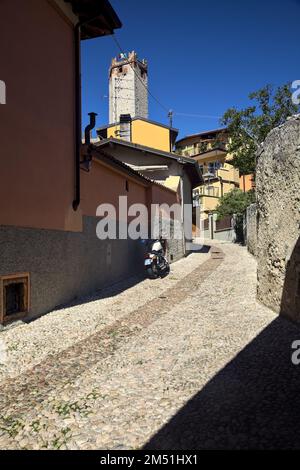 Tour du château de Scaligero encadrée par des bâtiments vus d'une place à l'entrée de Malcesine avec des magasins et des gens passant par Banque D'Images