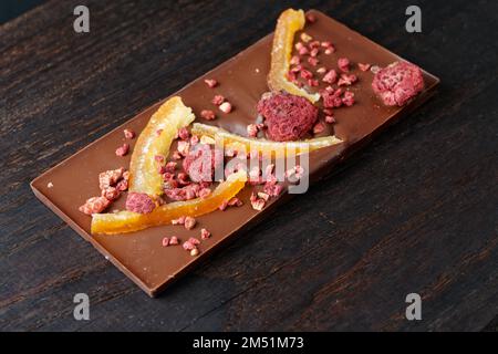 Barre de chocolat avec zeste d'orange confite et framboise sur planche à découper en bois sombre Banque D'Images