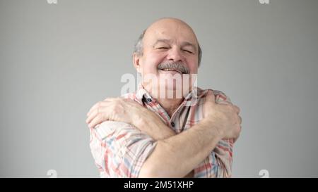 Homme âgé souriant et plein d'assurance se tenant près de lui-même, isolé sur fond de mur gris. Banque D'Images