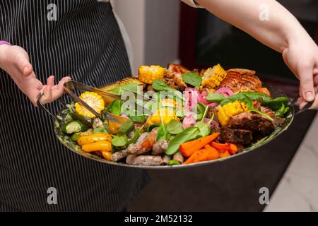 Le serveur a apporté un plat de viande et de légumes, frits dans un wok, mis sur un bol avec des coals chauds sur la table pour le garder chaud pendant longtemps Banque D'Images