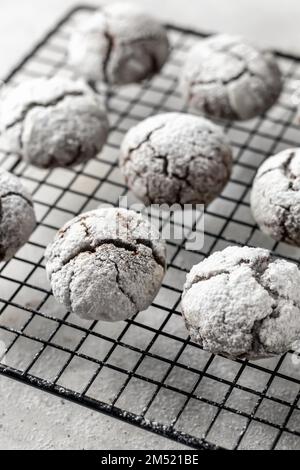 Biscuits aux pépites de chocolat avec fissures. Portoir métallique avec biscuits secs au chocolat frais dans du sucre glace sur fond texturé gris. Orientation verticale Banque D'Images