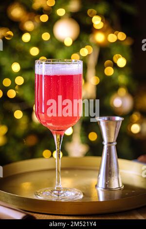 Cocktail rouge dans un verre élégant avec dose de cocktail. Illuminations de Noël en arrière-plan. Ambiance de fête et décoration de fête. Banque D'Images