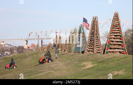 Gramercy, États-Unis. 23rd décembre 2022. Un couple d'hommes ont coupé de l'herbe dans une tondeuse à vélo tandis qu'un groupe de feux de camp sont alignés sur le lévee avec le pont commémoratif des anciens combattants en arrière-plan à Gramercy, Louisiane, vendredi, 23 décembre 2022. (Photo de Peter G. Forest/Sipa USA) crédit: SIPA USA/Alay Live News Banque D'Images