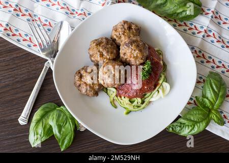 Vue de dessus des boulettes de viande avec sauce tomate et des griboulis sur une assiette blanche à côté d'une fourchette et d'une cuillère sur une table en bois Banque D'Images