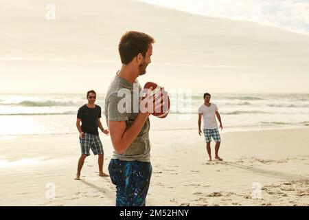 Se mettre en forme de manière ludique. un groupe de jeunes amis heureux jouant avec une balle sur la plage. Banque D'Images