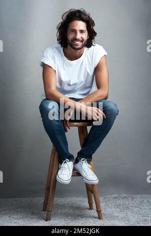 Maintenant, je passe au niveau supérieur. Photo studio d'un beau jeune homme assis sur un tabouret sur un fond gris. Banque D'Images