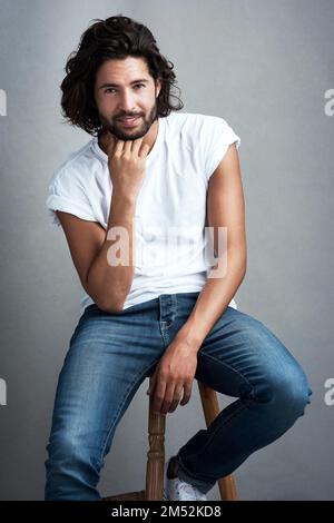 Rien ne semble mieux que la confiance. Photo studio d'un beau jeune homme assis sur un tabouret sur un fond gris.