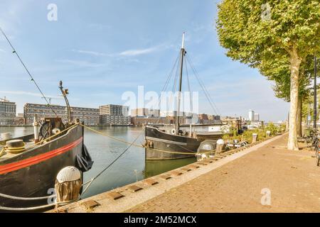 deux bateaux amarrés dans l'eau avec des bâtiments en arrière-plan et des personnes marchant sur le trottoir à côté des autres bateaux Banque D'Images