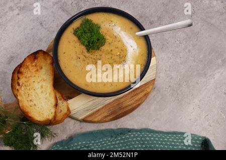 purée de soupe aux lentilles rouges dans un bol sombre avec du pain sur une table en marbre gris Banque D'Images