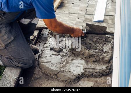 Le calque de briques pose des carreaux. Un constructeur professionnel en combinaison et casquette de baseball au travail. Maçon âgé travaillant à l'extérieur. Gros plan... Banque D'Images