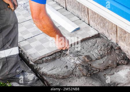 Le calque de briques pose des carreaux. Un constructeur professionnel en combinaison et casquette de baseball au travail. Maçon âgé travaillant à l'extérieur. Gros plan... Banque D'Images