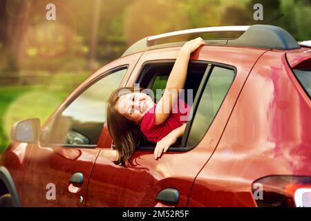 Se mettre un peu agité sur le siège arrière. Portrait d'une adorable petite fille penchée hors d'une fenêtre de voiture à l'extérieur. Banque D'Images