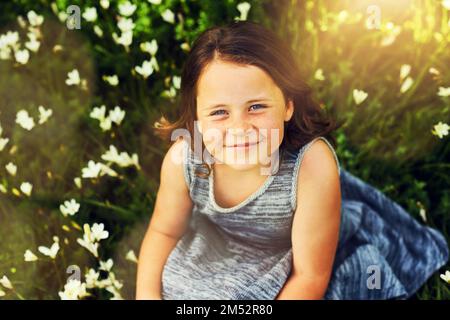 J'appartient entre les fleurs. Portrait d'une petite fille douce assise dans un champ de fleurs sauvages. Banque D'Images