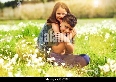 Les frères et sœurs partagent un lien spécial. Portrait d'une petite fille mignonne donnant à son grand frère un câlin à l'extérieur. Banque D'Images