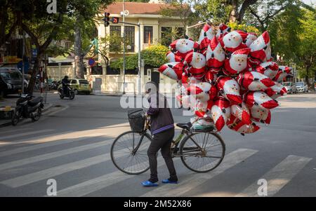 Un vendeur de rue pousse sa bicyclette chargée de ballons de noël de père de l'autre côté d'une rue dans le quartier français de Hanoi, Vietnam. Banque D'Images