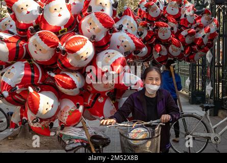 Un vendeur de rue pousse sa bicyclette chargée de ballons de noël de père à Hanoi, Vietnam. Banque D'Images